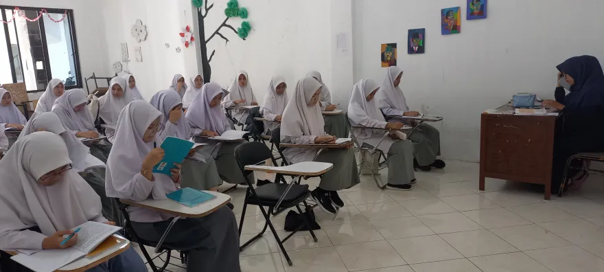Santri putri berhijab menulis di meja ruang kelas
